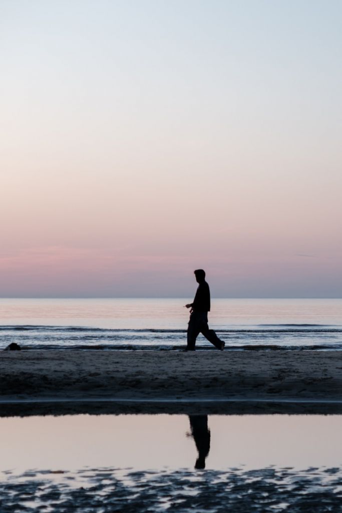 Person walks on beach during sunset.